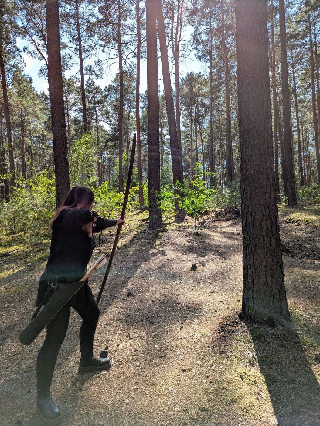 Bogenschützin zwischen hohen Kiefern auf einem Waldweg