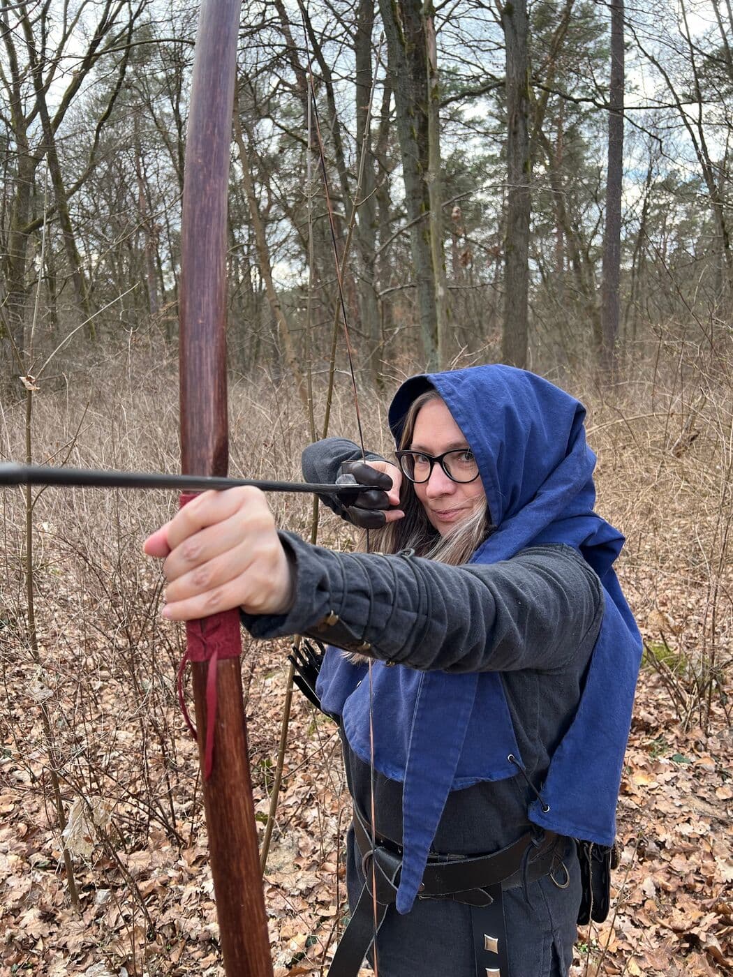 Bogenschützin in mittelalterlicher Gewandung mit blauer Gugel beim Zielen
